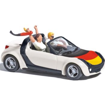 Smart Roadster, Fußball Fieber 2024, mit Fahrer und Beifahrerin mit Deutschlandschal und Deutschlandfahne auf der Motorhaube
