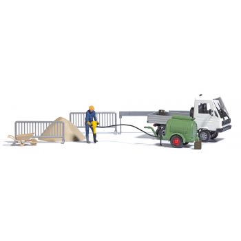 Kompressor mit Presslufthammer. Bauarbeiter mit Presslufthammer, Multicar Pritschenfahrzeug, Kanistern, Absperrungen, Sandhaufen und Schubkarren.