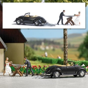 Action Set Hochzeit, Braut und Bräutigamm, die traditionell einen Baumstamm zersägen, mit VW Hebmüller Cabrio als Hochzeitsfahrzeug