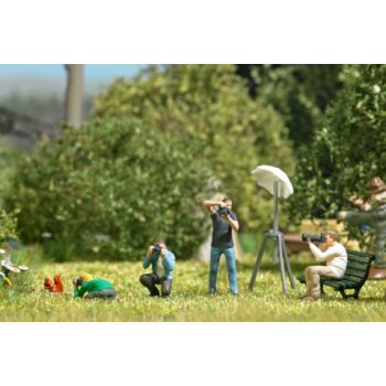 4 Fotografen in unterschiedlichen Positionen mit Kameras. Studioscheinwerfer, Dekoration, Holzkisten, Vogelscheuche, Kleintiere, Aliens, Blumen, Bänke