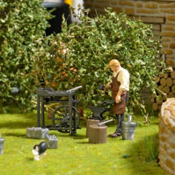 Feldschmiede, der Schmied bearbeitet auf dem Amboss ein Hufeisen. Action-Set mit Schmied, Feldschmiede, Amboss, 2 Hackstöcken, Säcken, Holzstapel,